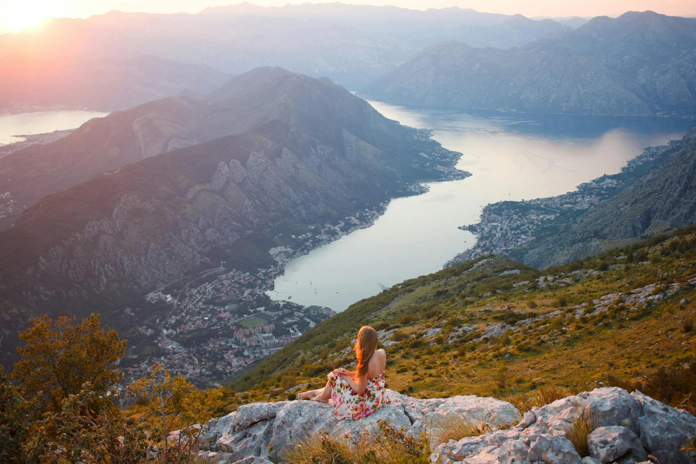 a woman sitting on top of a mountain overlooking a lake