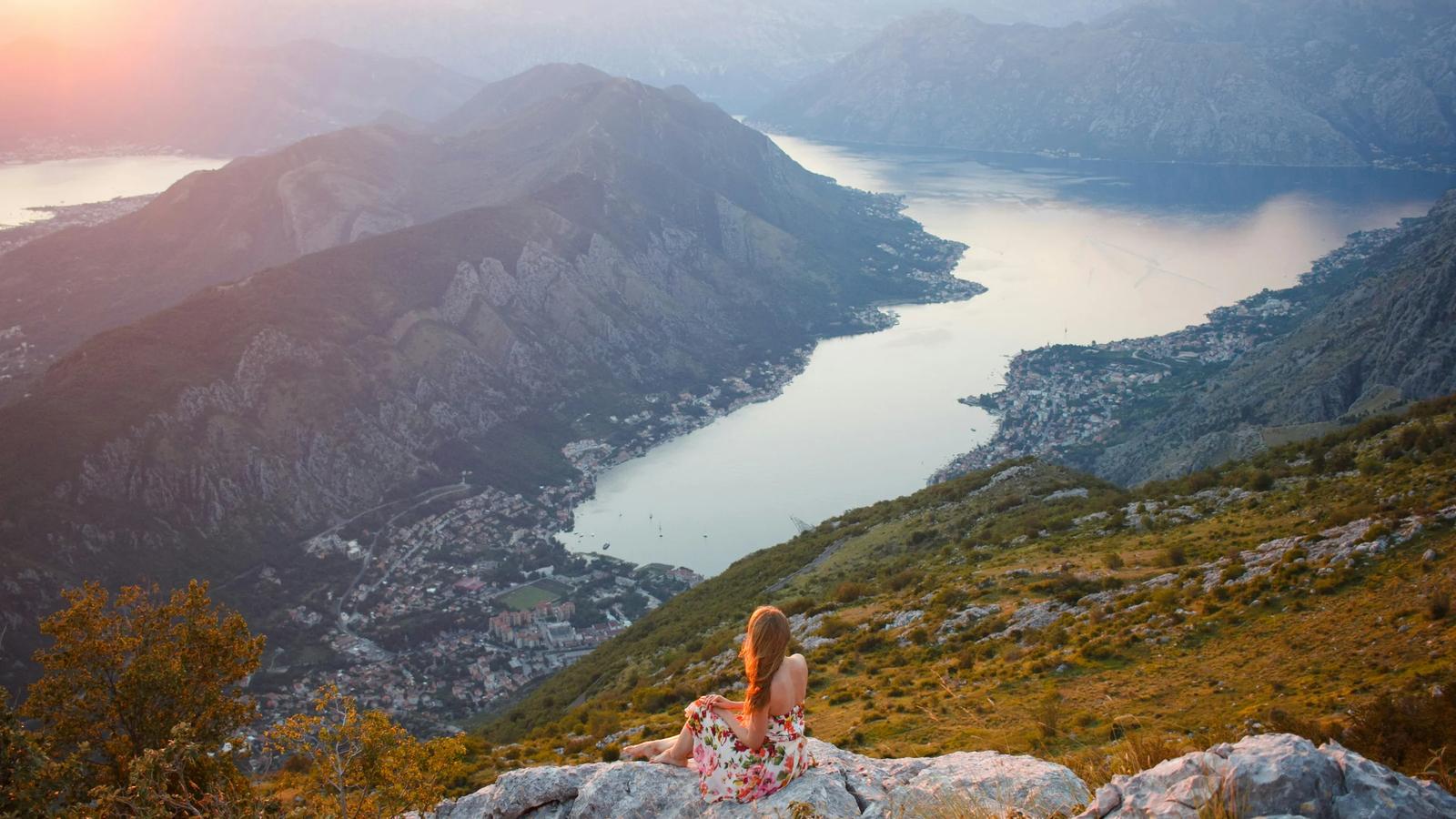 a woman sitting on top of a mountain overlooking a lake