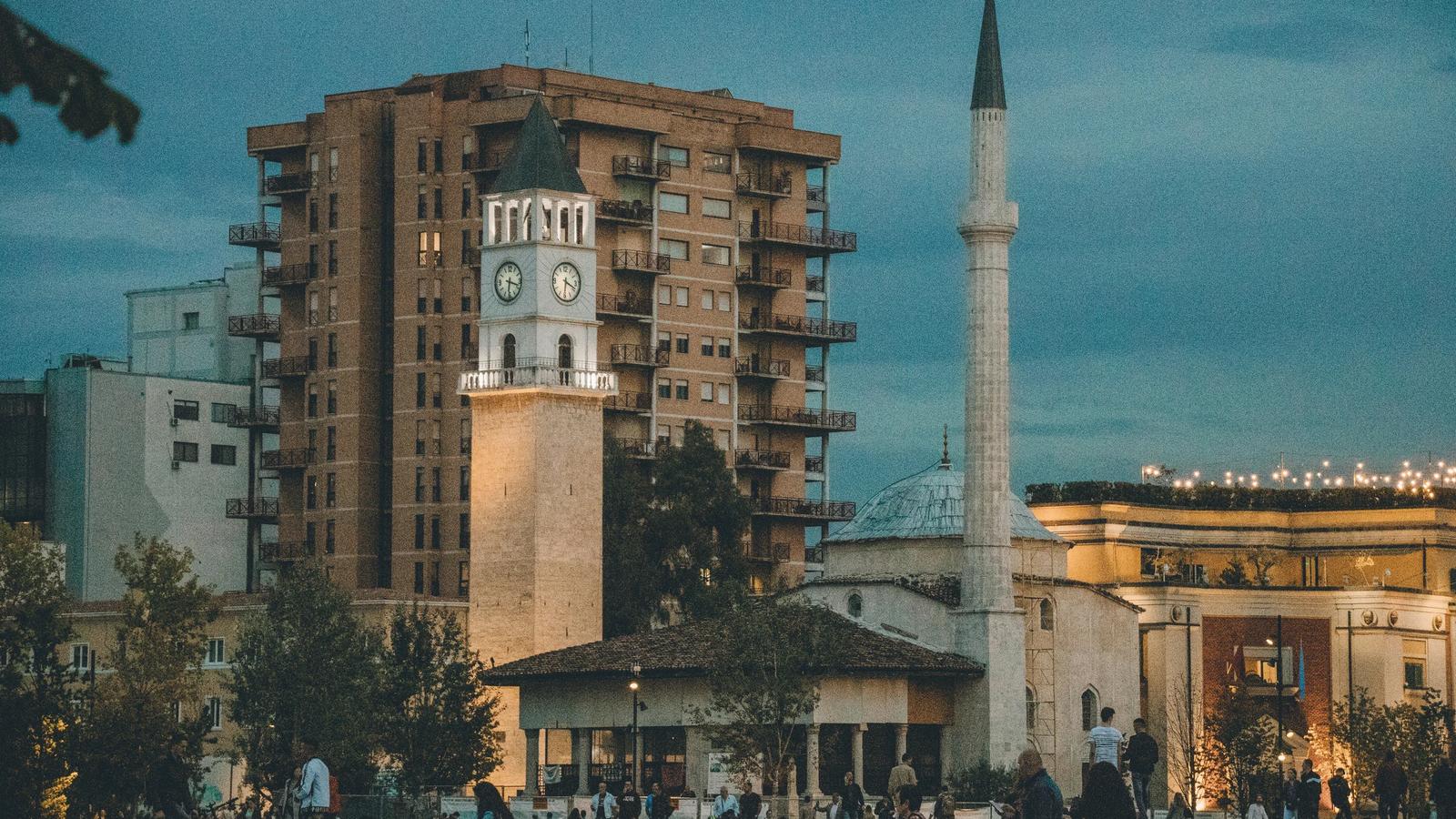 a group of people walking around a plaza with a clock tower in the background