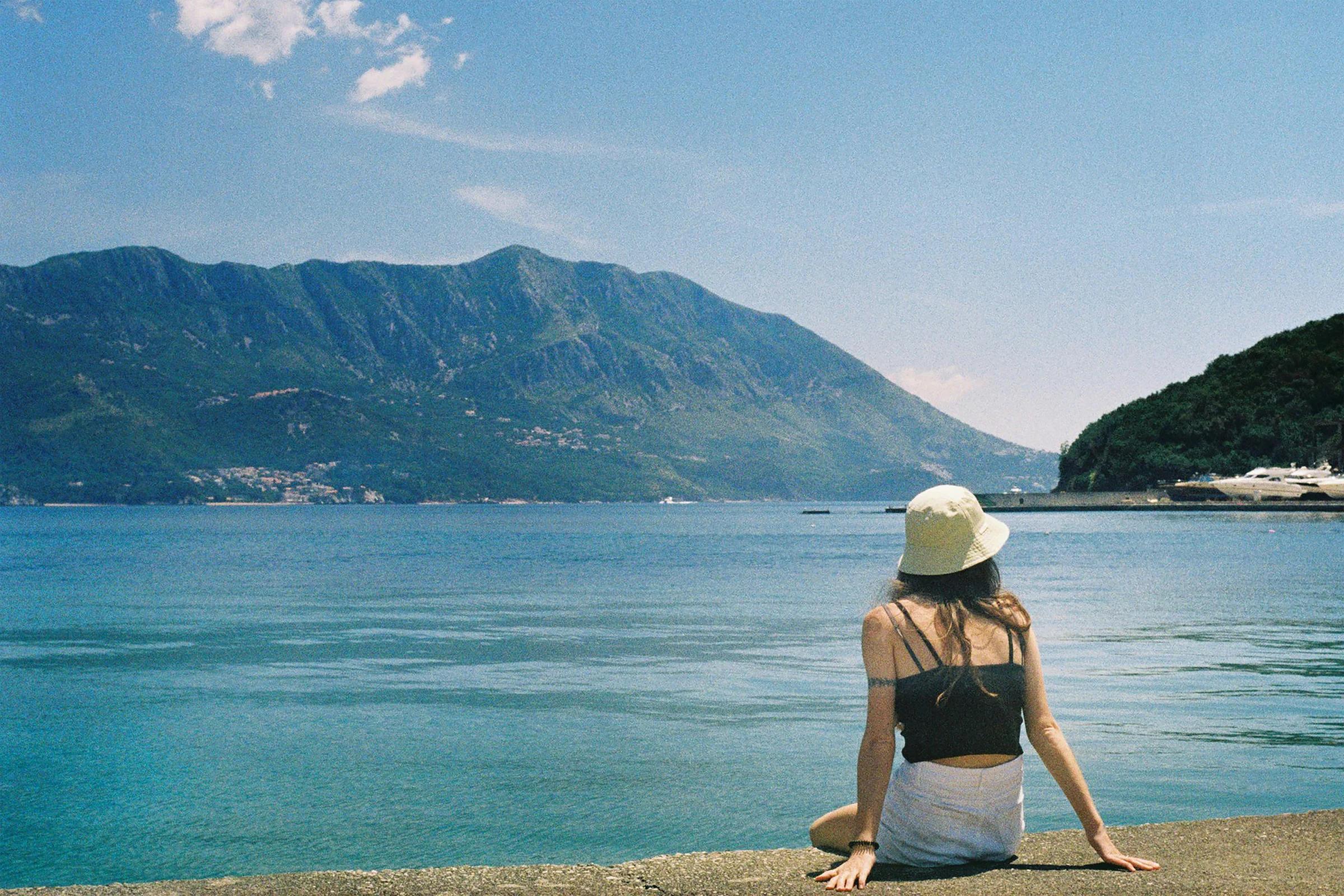 Woman in hat looking at scenic ocean and mountains