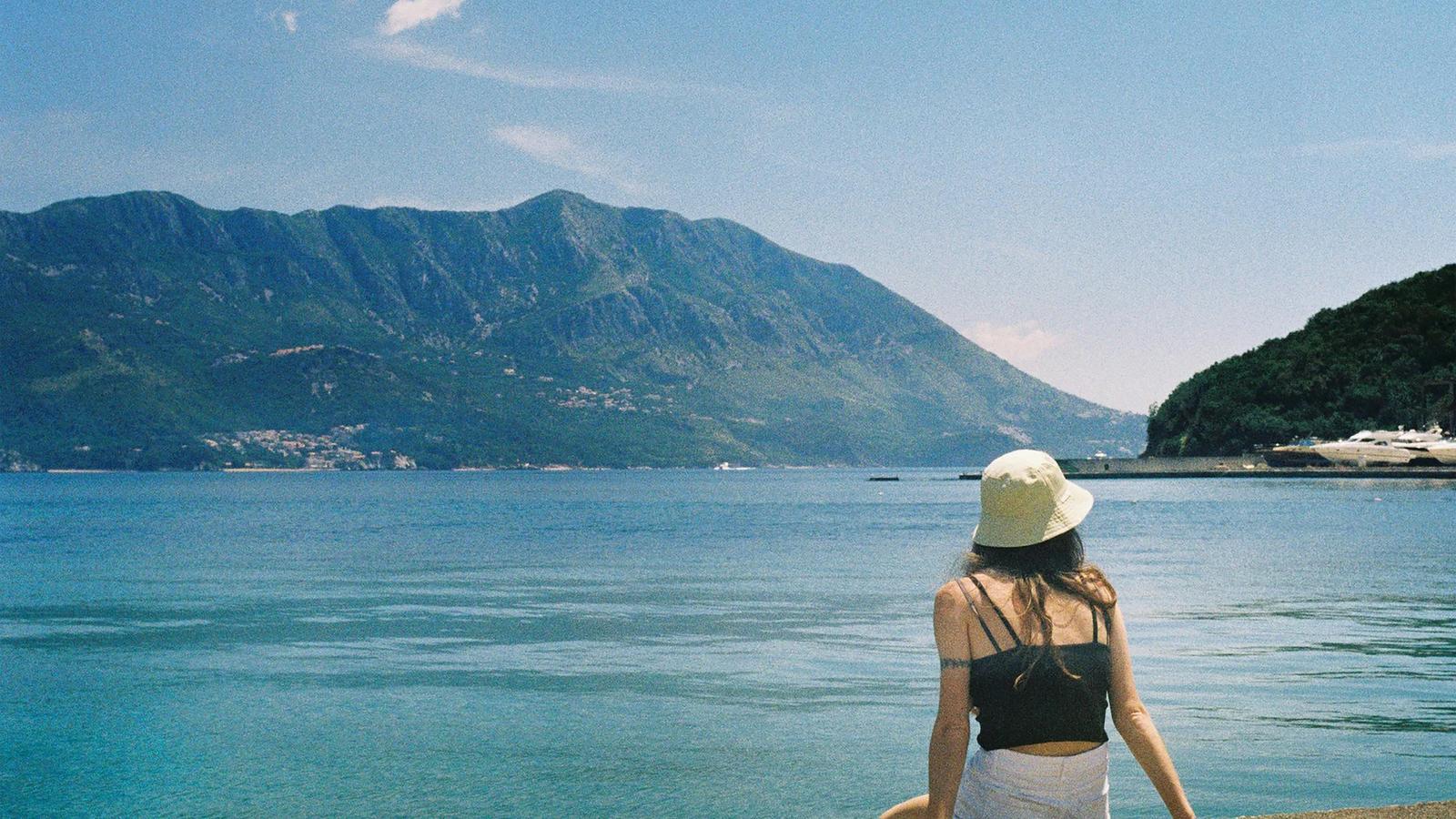 Woman in hat looking at scenic ocean and mountains