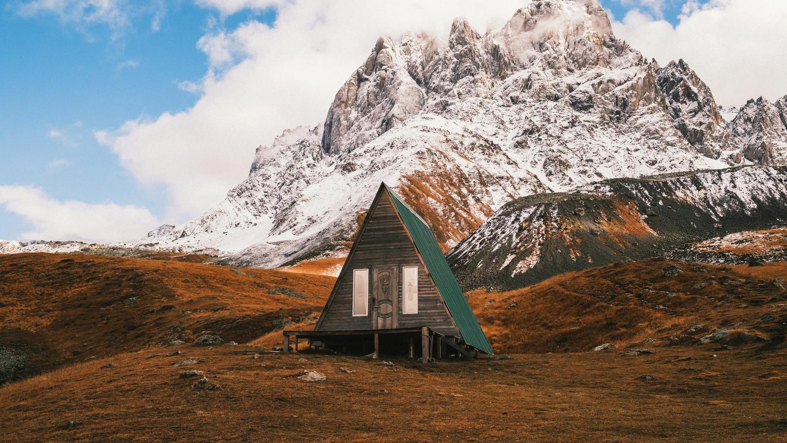 a cabin in the middle of a field with a mountain in the background