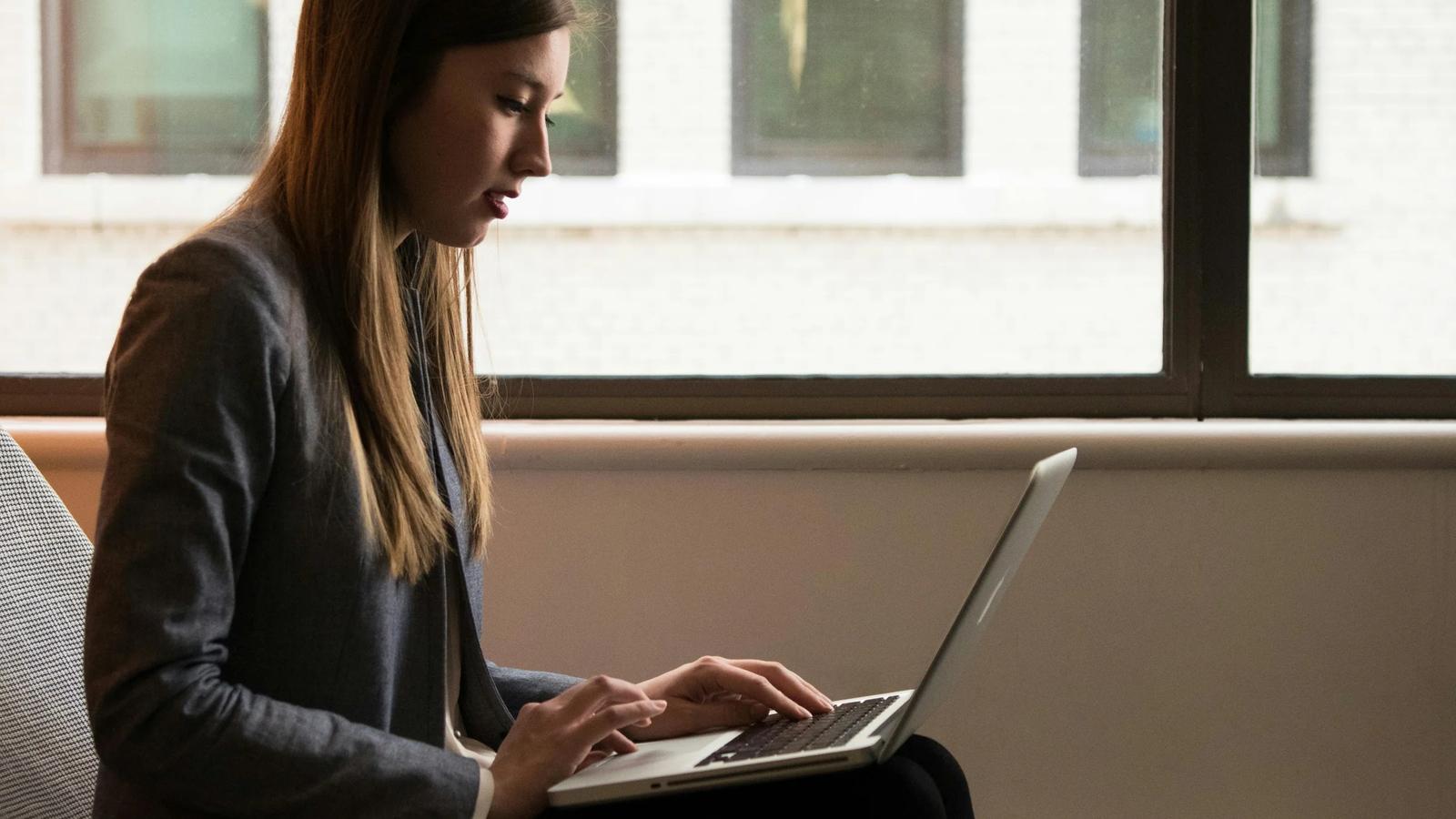 Женщина сидит и использует ноутбук на коленях