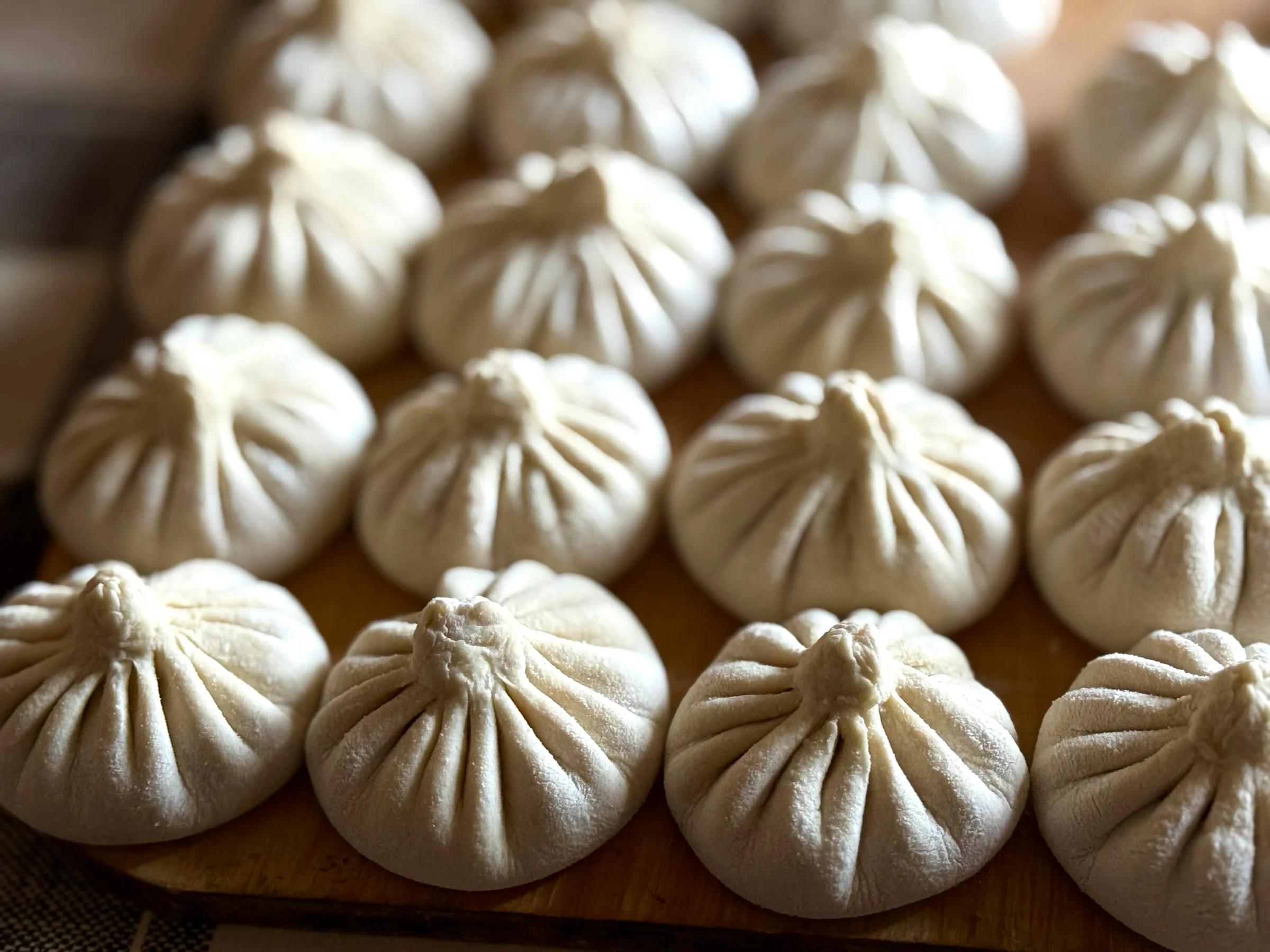 Крупный план свежеприготовленных пельменей на подносе.