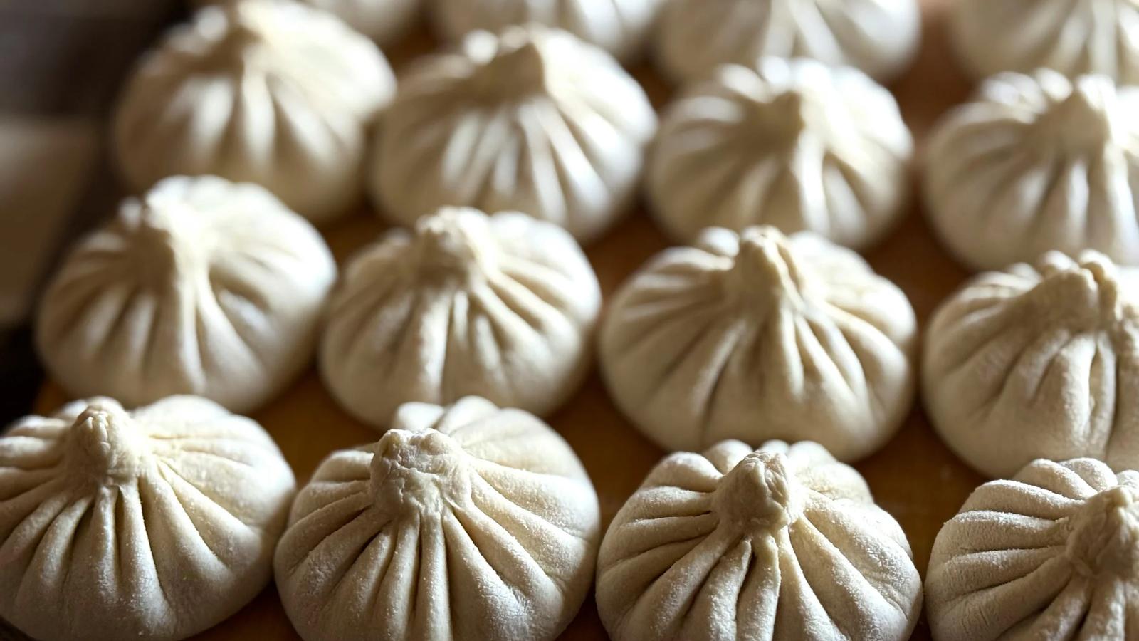 Крупный план свежеприготовленных пельменей на подносе.