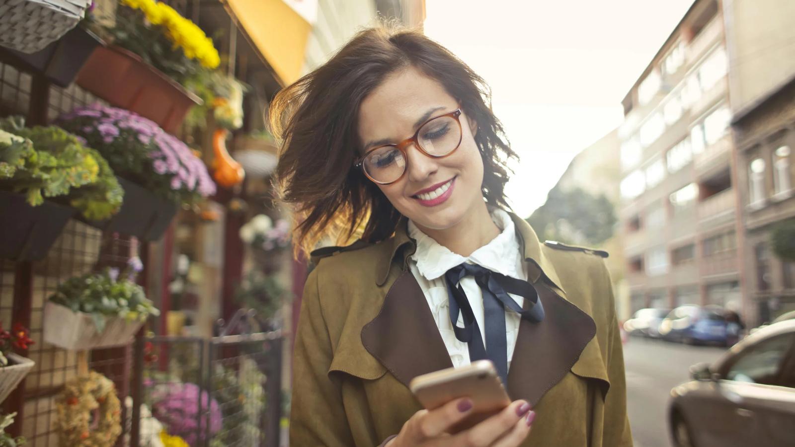 Женщина рядом с цветочным магазином с помощью смартфона