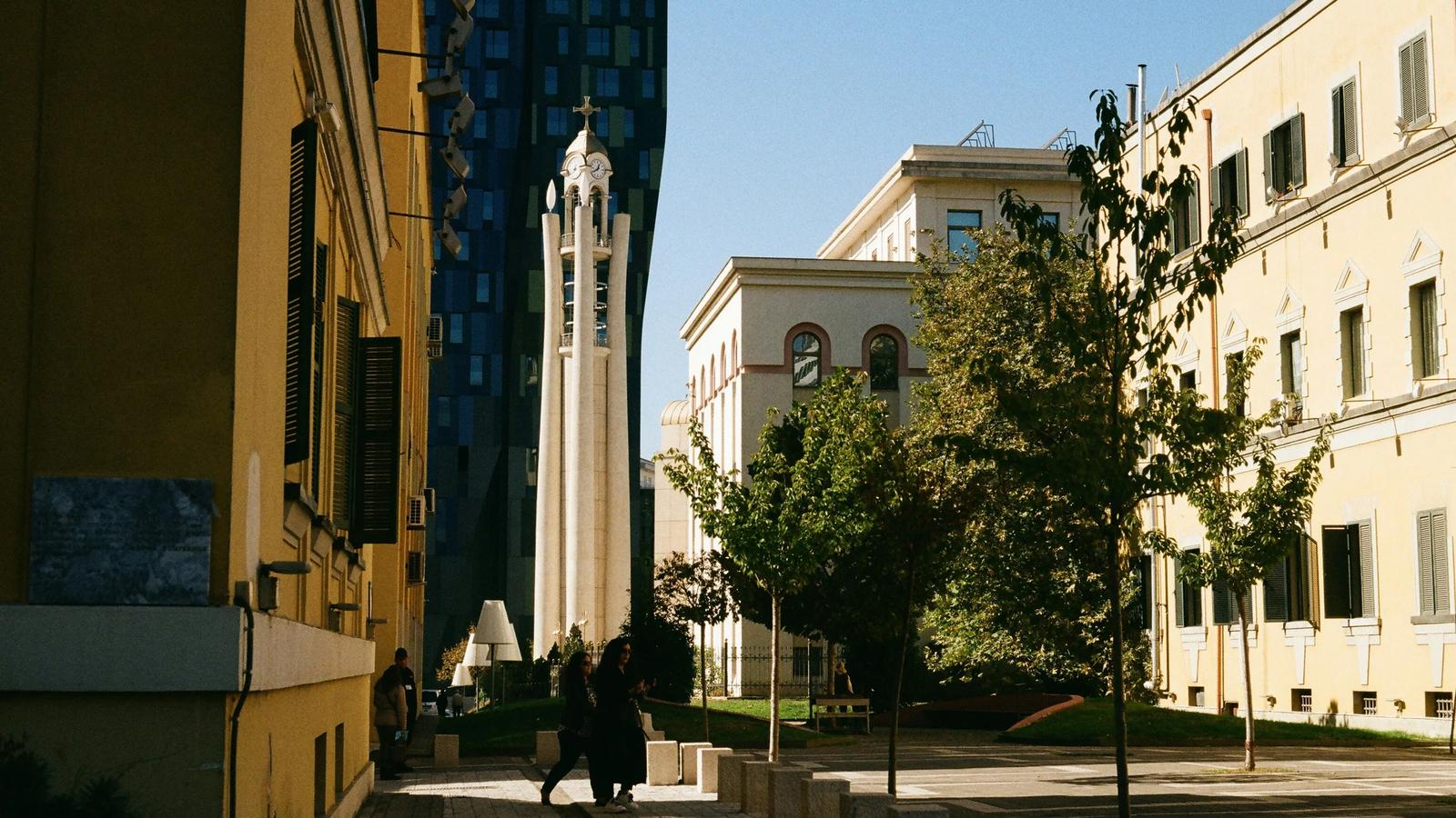 a couple of people walking down a street next to tall buildings