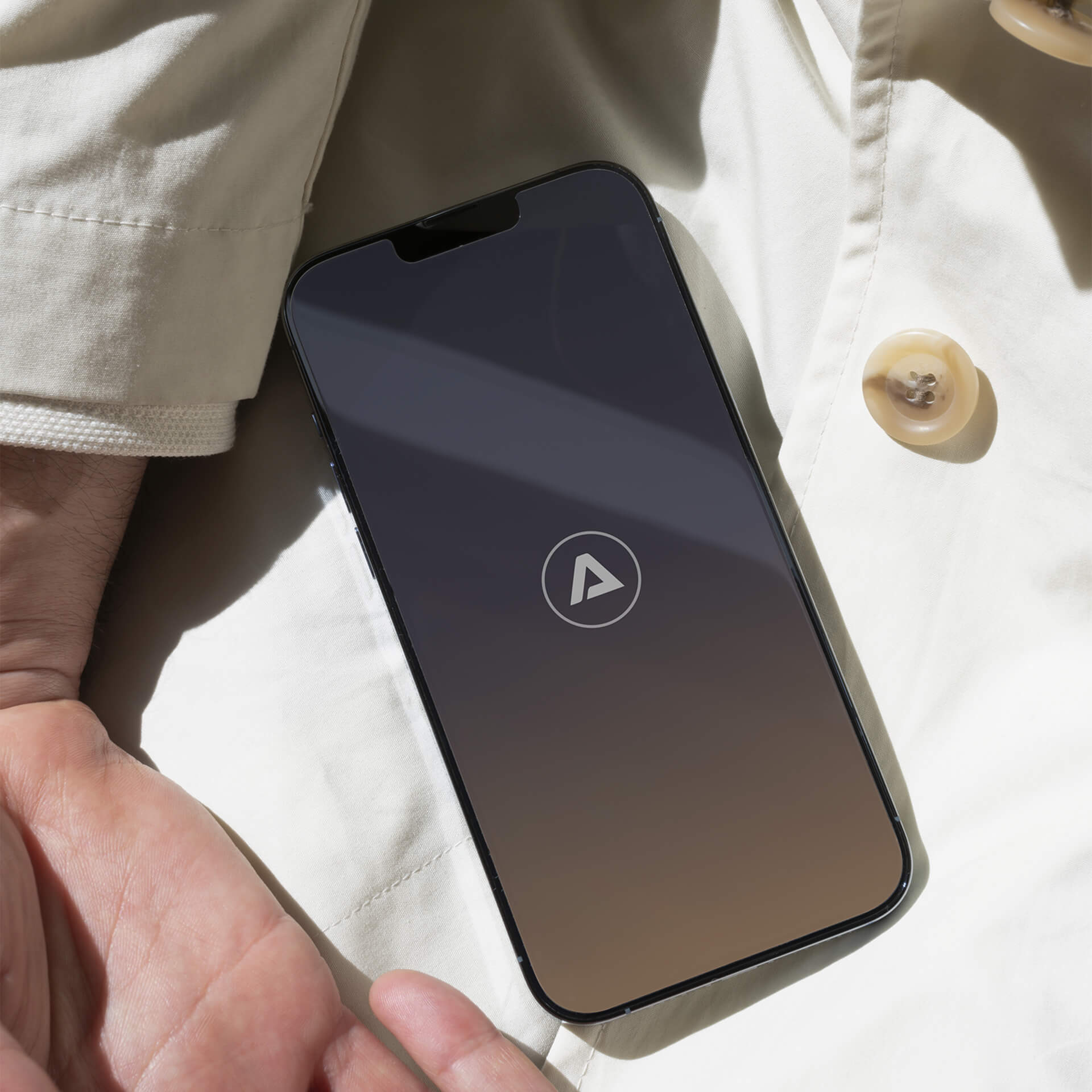 Close-up photo of a smartphone atop a cream-coloured garment. The phone shows a dark startup screen with the circular Abloxx logo at the center.