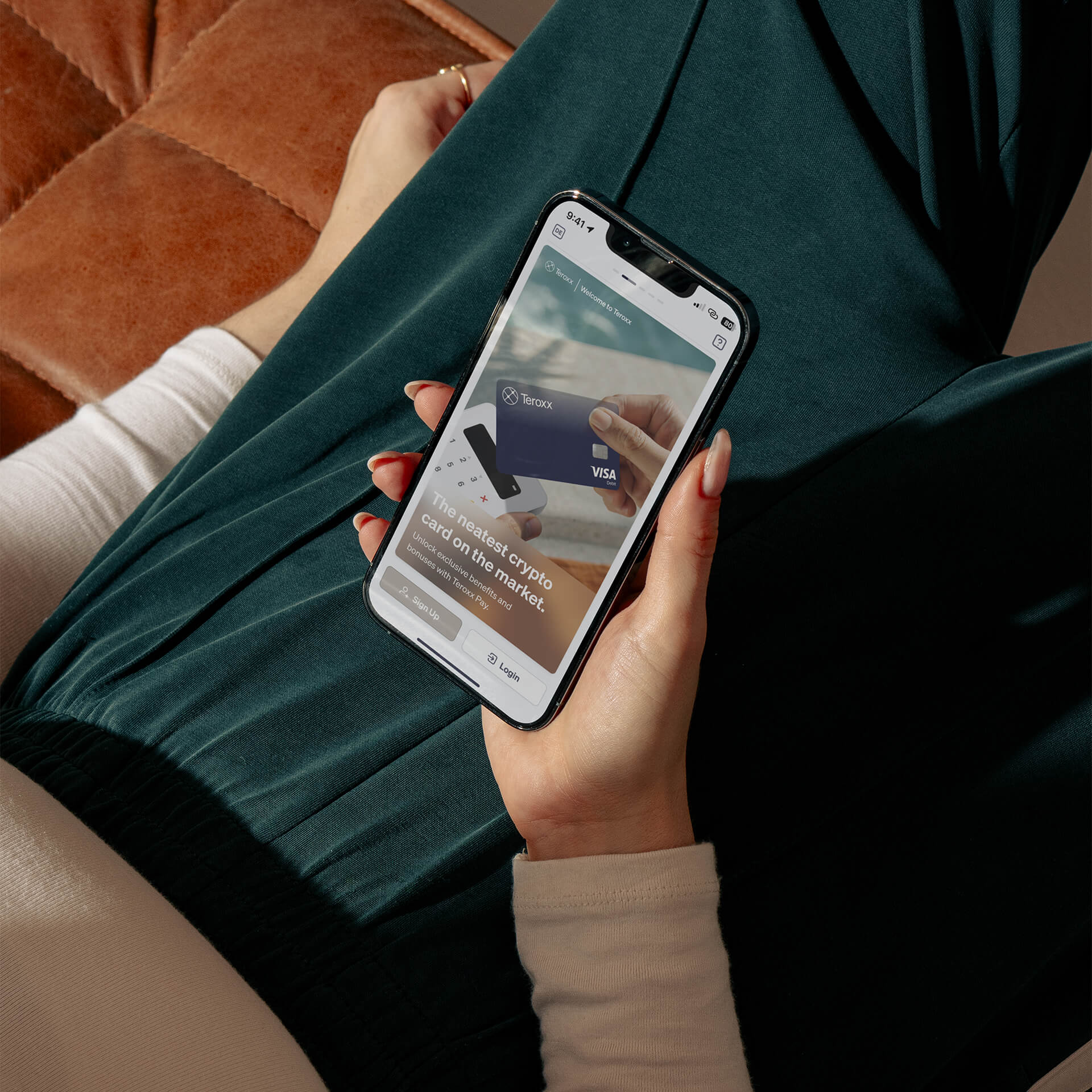 Photo of a woman holding a smartphone in her lap. The screen shows a Teroxx-branded Visa card with the text ‘The neatest crypto card on the market’.
