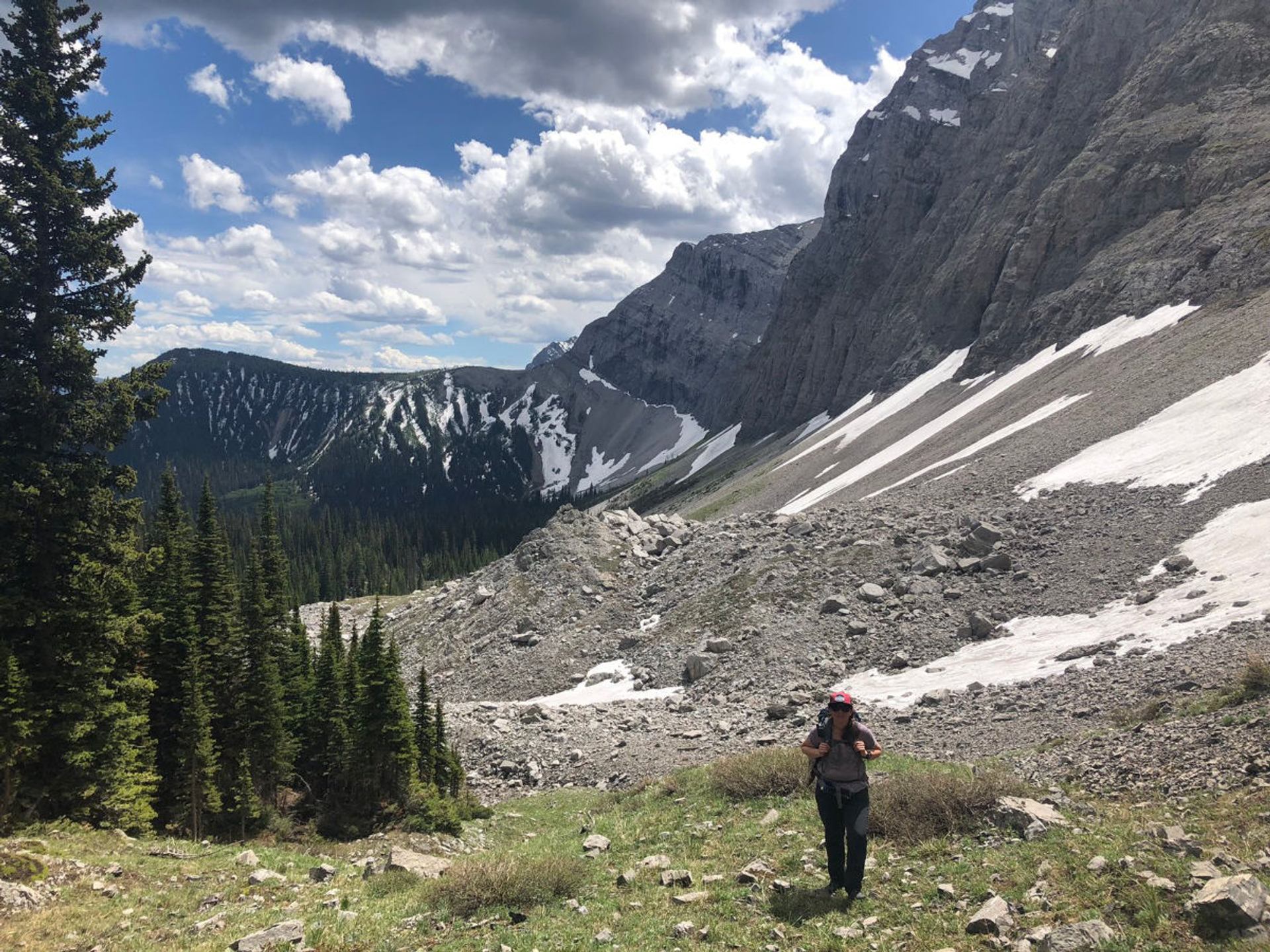 A backpacker walking through a rocky alpine basin with steep cliffs and scattered snow.