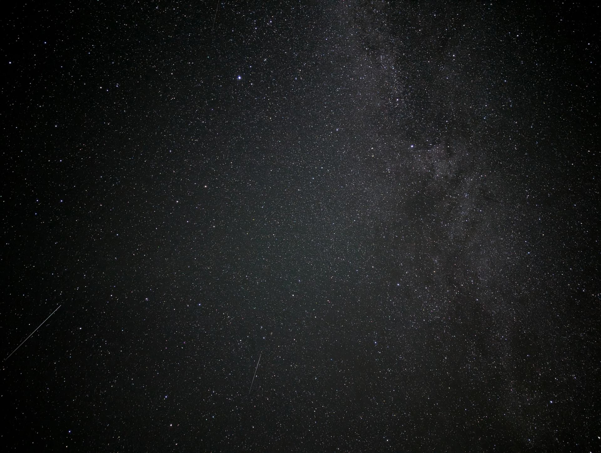Night sky filled with countless stars and faint streaks of light from meteors.