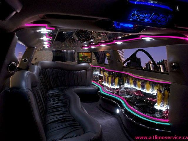 Luxurious limo interior with black leather seats, neon lights, and a bar with glasses and bottles.