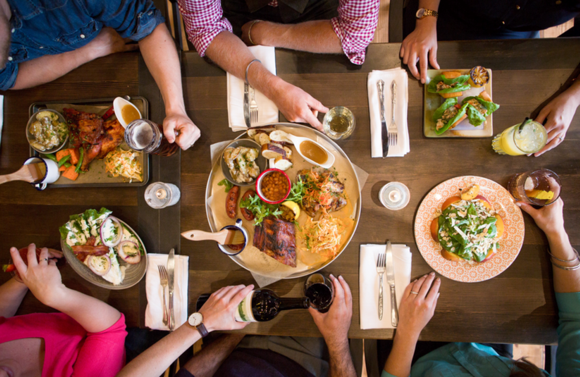 Overhead view of a group of people sharing a large meal with multiple dishes on a wooden table.
