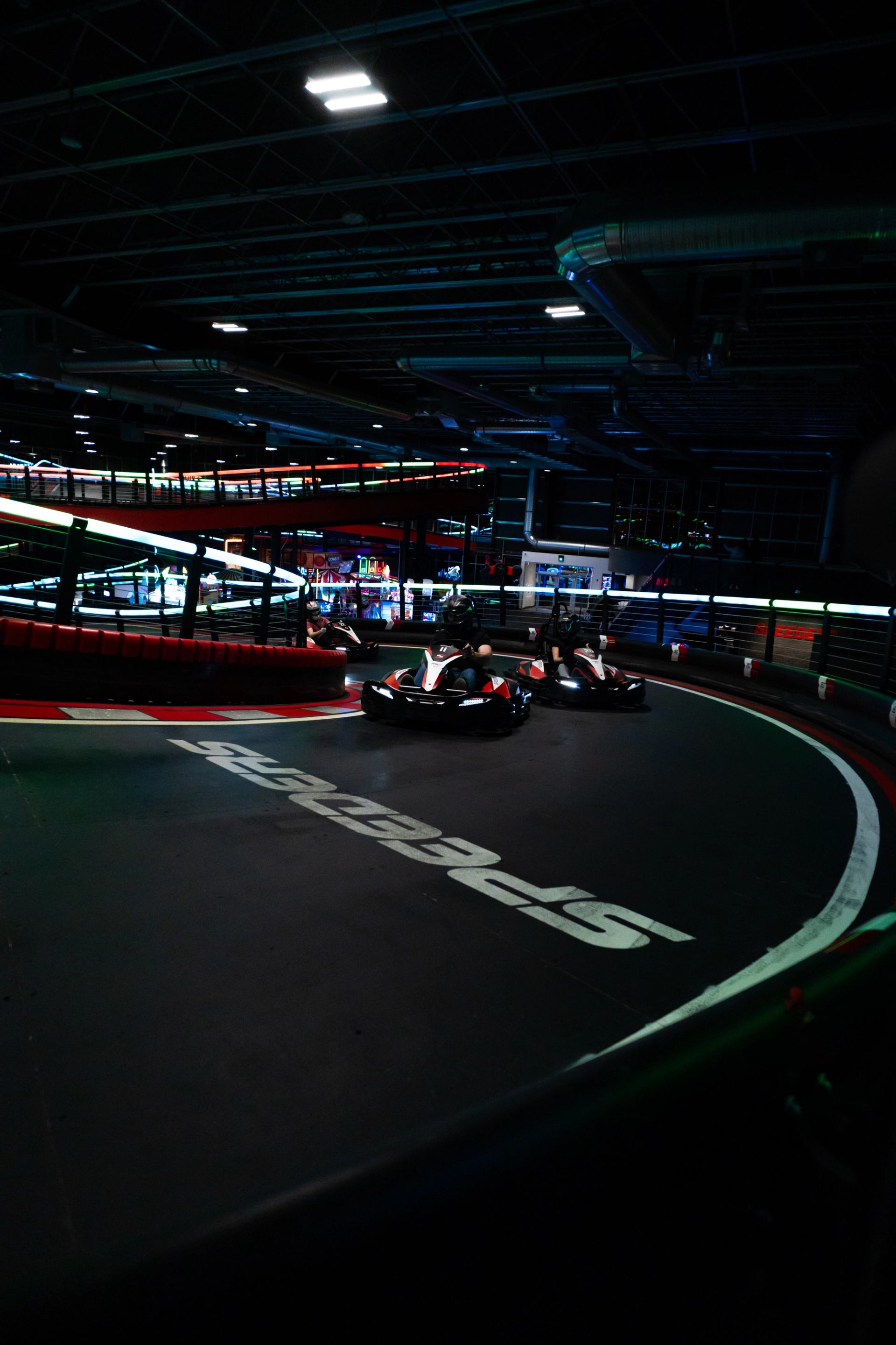 Go-kart racing on a dark indoor track with glowing lights and sharp curves at Speeders.