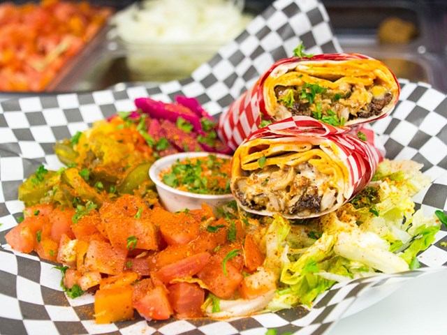 Colorful Mediterranean wrap with sides of veggies, sauce, and pickled garnishes.