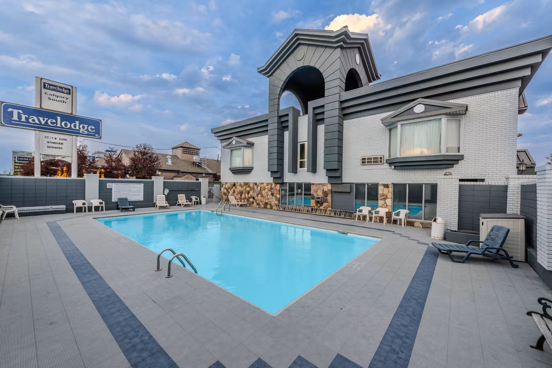 Travelodge Calgary South features an outdoor pool with lounge seating beside the hotel building.