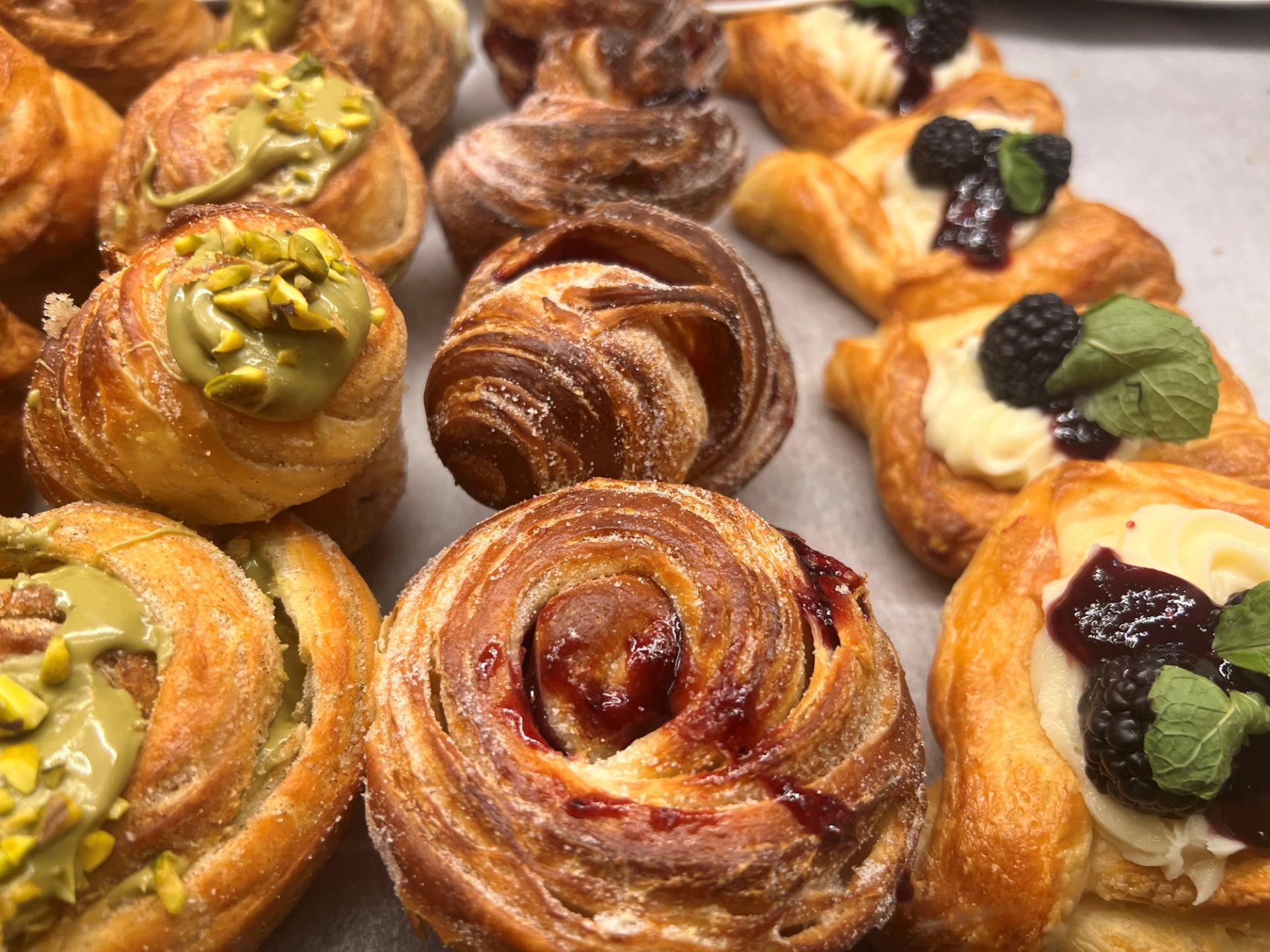 Assorted pastries with icing, pistachios, berries, and caramel on a tray.