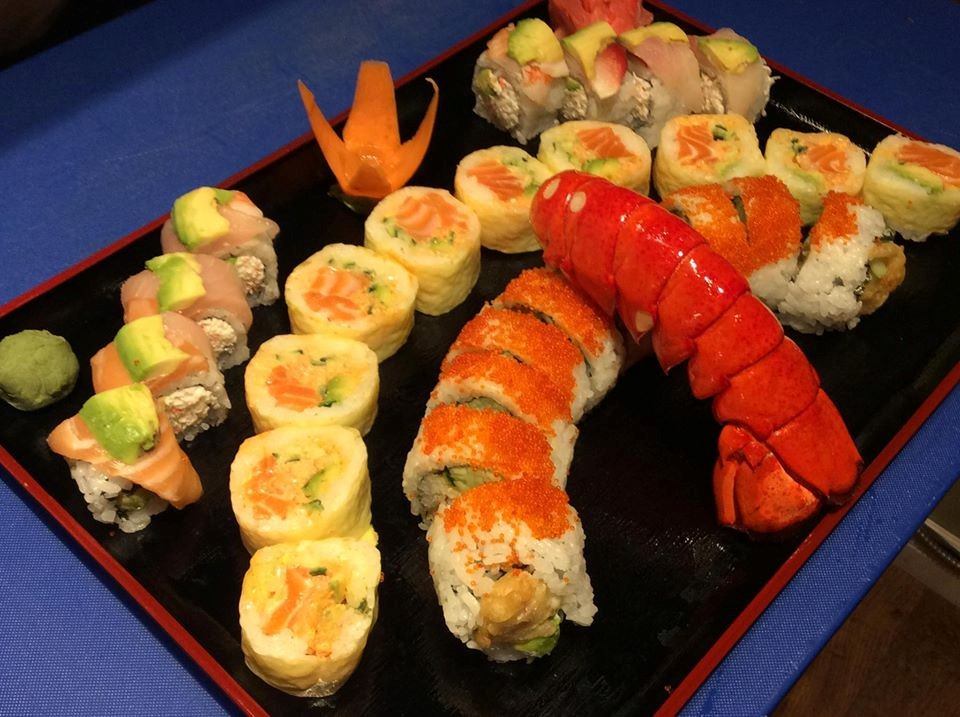 Variety of sushi rolls with avocado, fish, and roe on a black tray