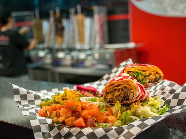 Cut wrap with meat and veggies, served with tomatoes and lettuce on checkered paper.