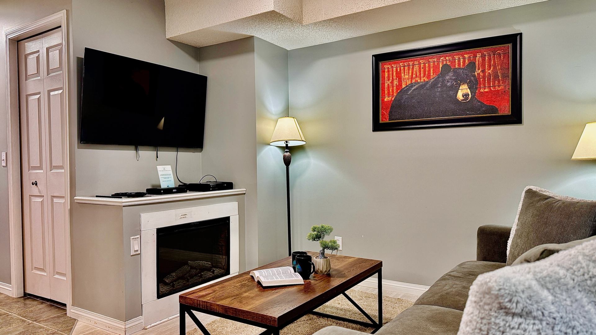Living room with fireplace, wall-mounted television, sofa, coffee table and framed bear artwork.
