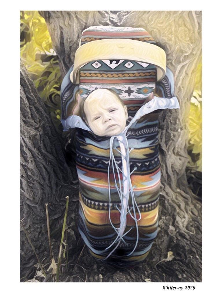 Baby doll wearing patterned Indigenous-style clothing, swaddled with white blanket and blue strings.