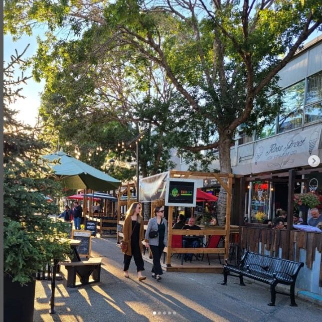 Sunny sidewalk scene with trees, benches, and a digital screen.