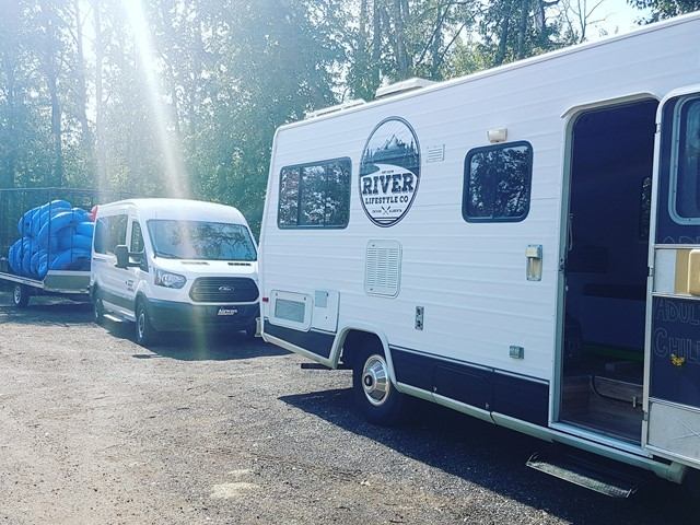 River Lifestyle Co. camper and van parked in a sunny forest setting with gear trailer.