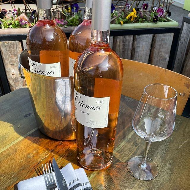 Rosé wine bottles in an ice bucket on an outdoor table with flowers and cutlery.