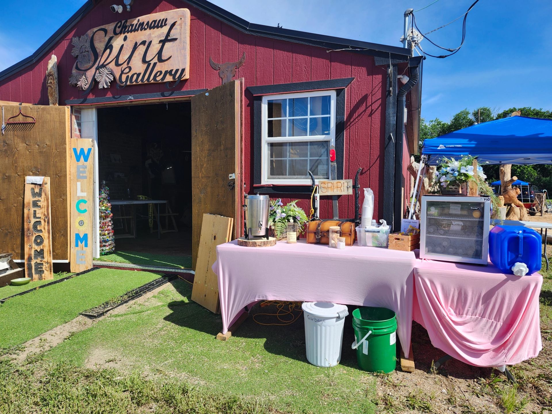 Outdoor view of Chainsaw Spirit Gallery with welcome signs and refreshment table.