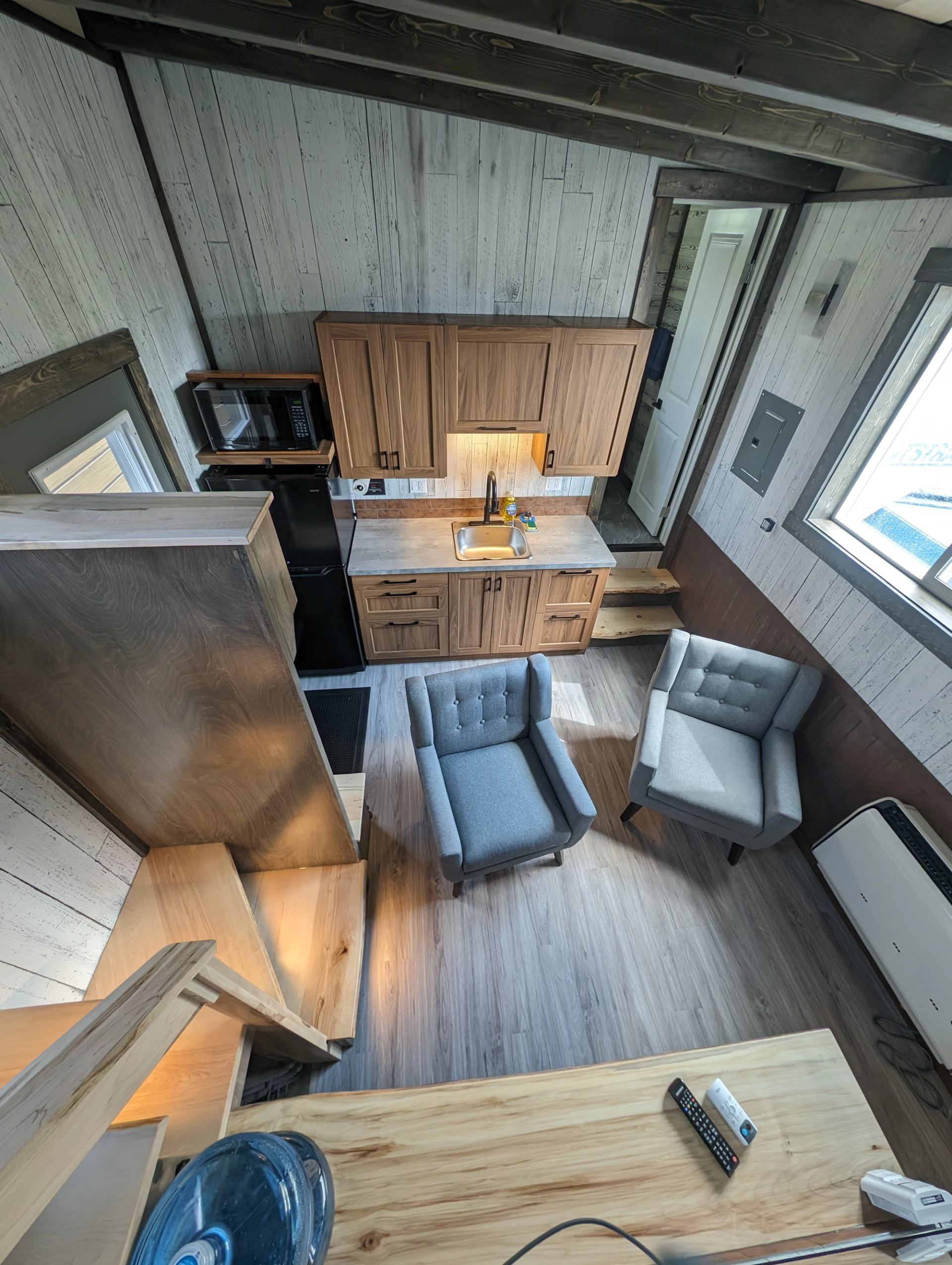 Compact interior with wood kitchen cabinets, two grey chairs and loft stairs.