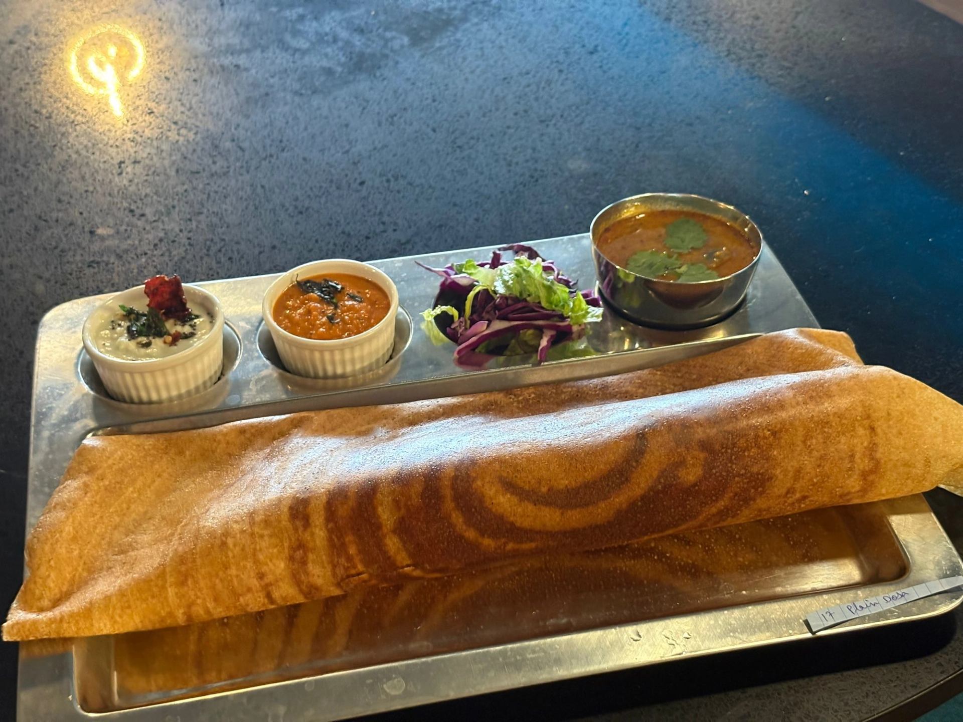 Crispy dosa served with chutneys, sambar, and fresh greens on a metal tray.