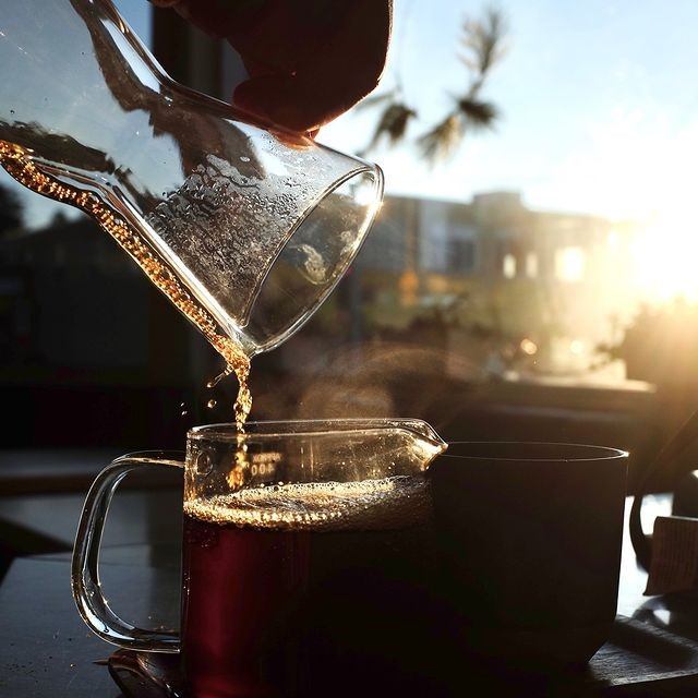 Coffee poured from a glass carafe into a mug with sunlight in the background.