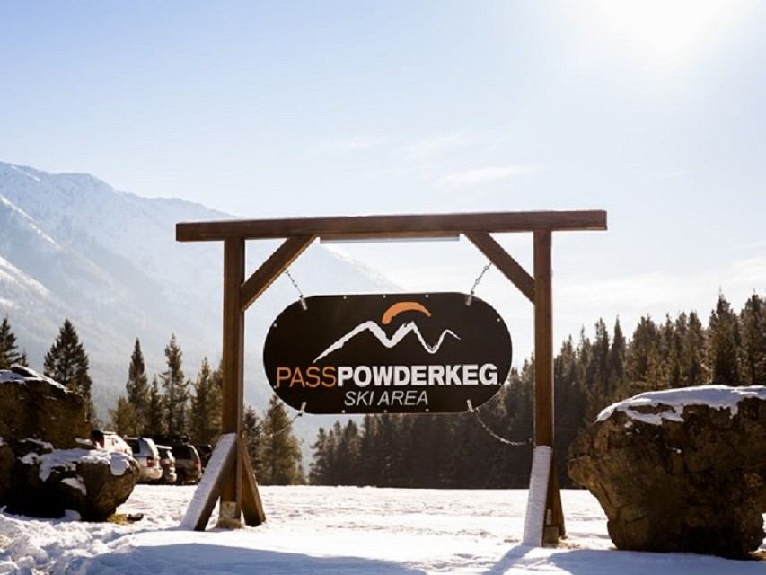 Pass Powderkeg Ski Area sign with snowy mountains and trees in the background.