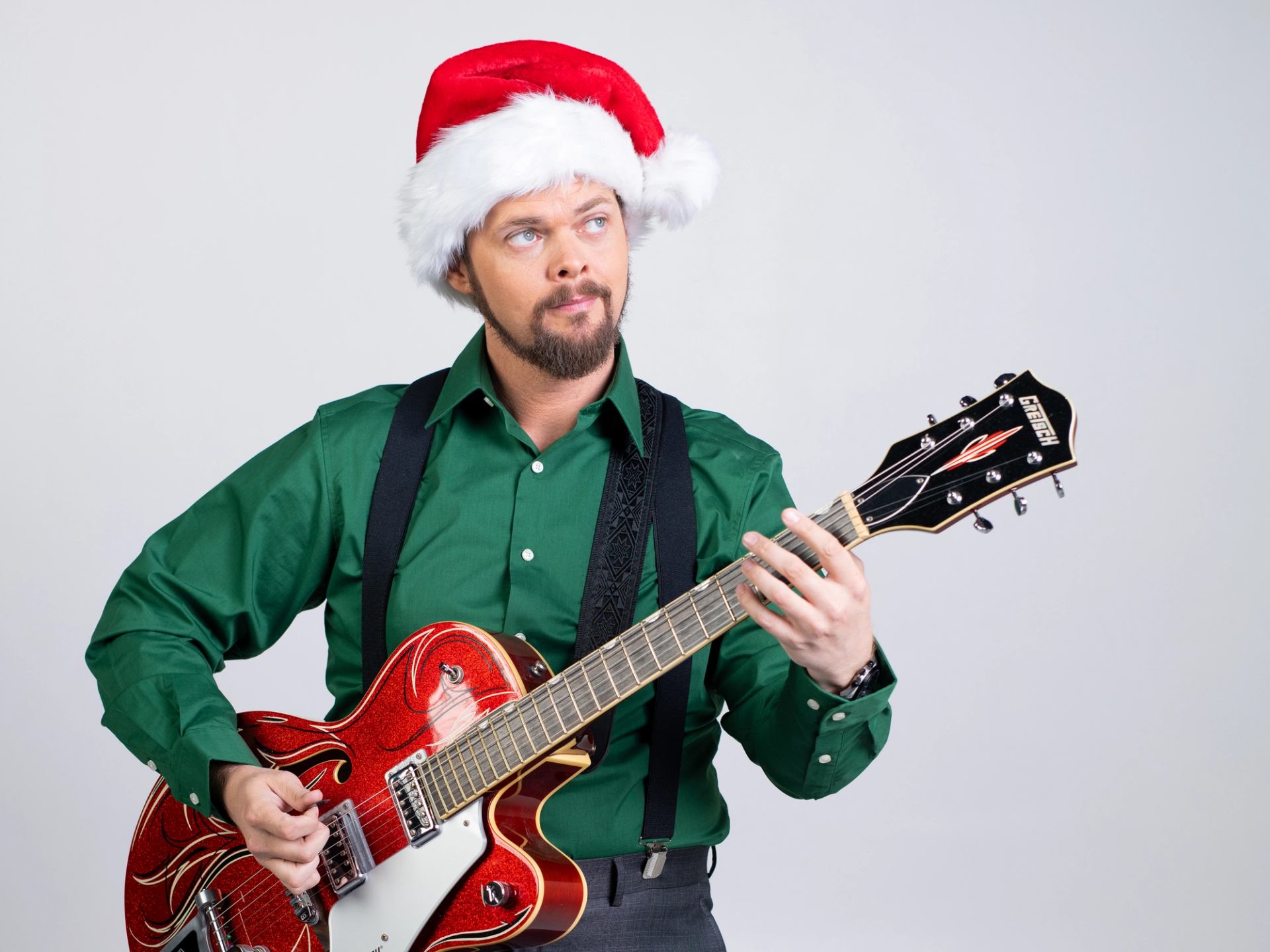 Person in a Santa hat playing a red electric guitar in festive attire.