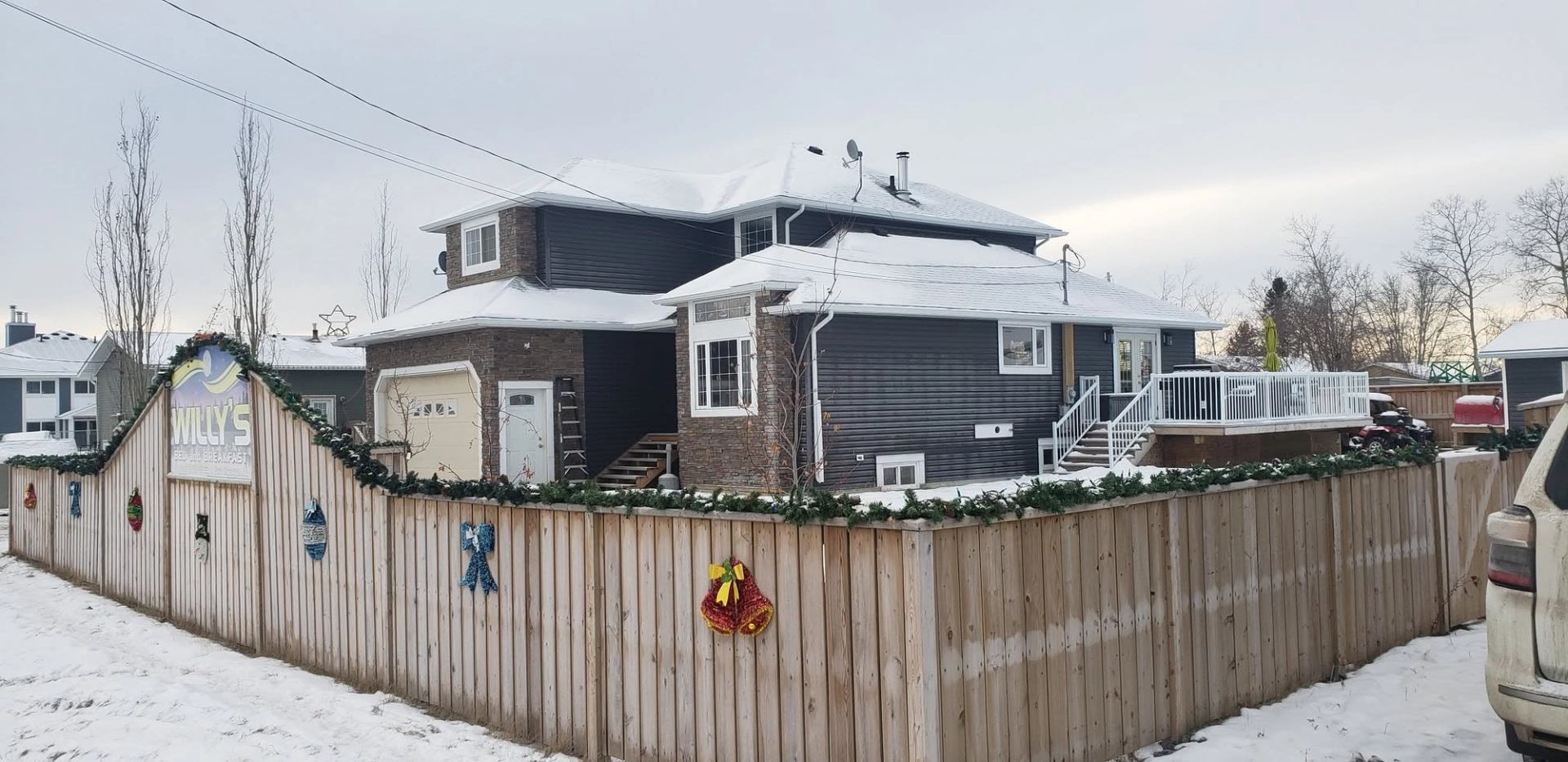 Snow-covered Willy’s Bed and Breakfast behind wooden fence with holiday decorations and garlands.