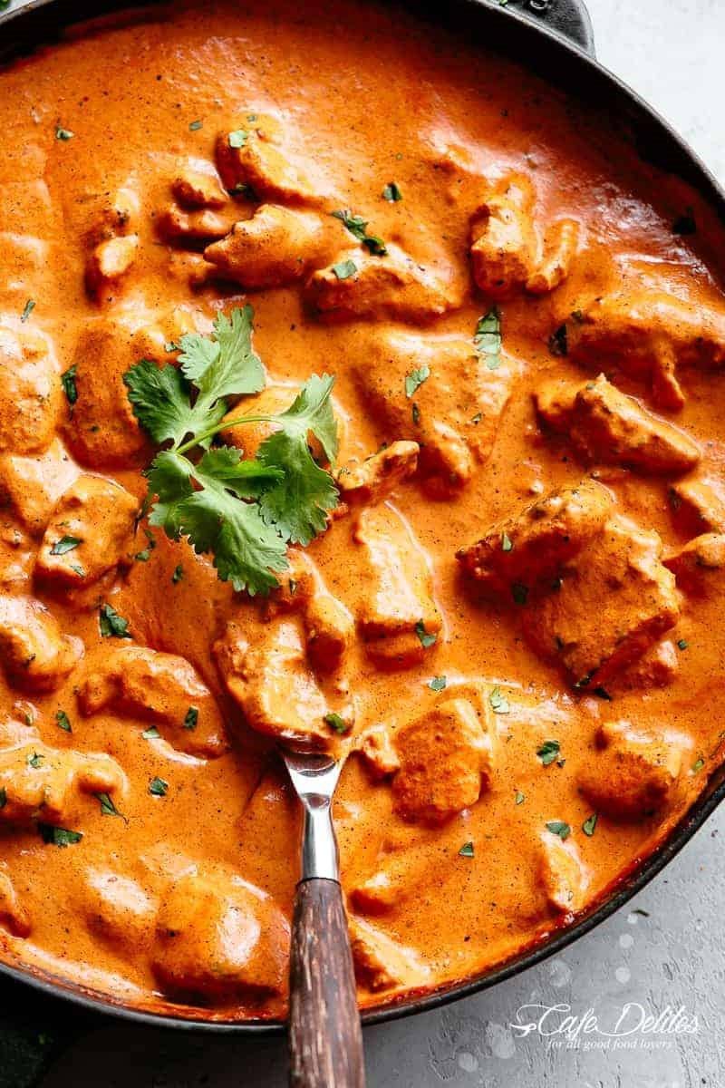 Kashmiri curry with meat in orange-red sauce, garnished with cilantro in a dark bowl with spoon.