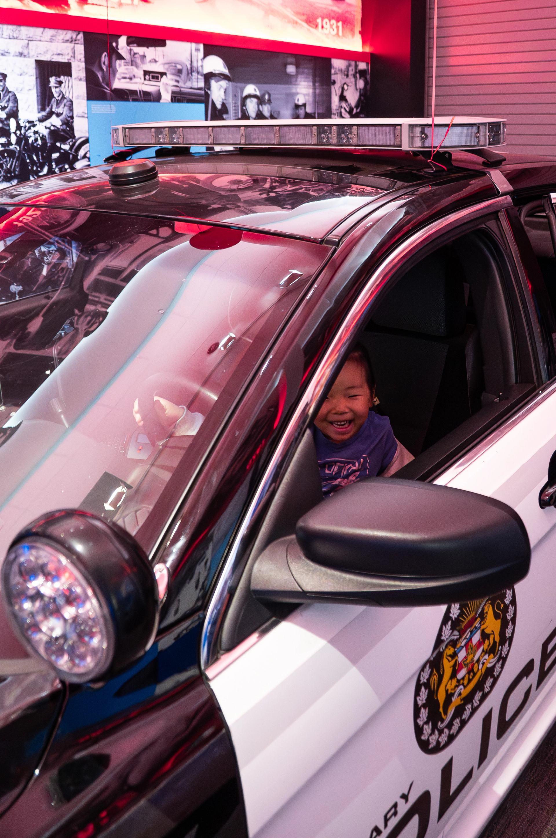 Child sits inside marked Calgary police car with red interior lighting and displays.