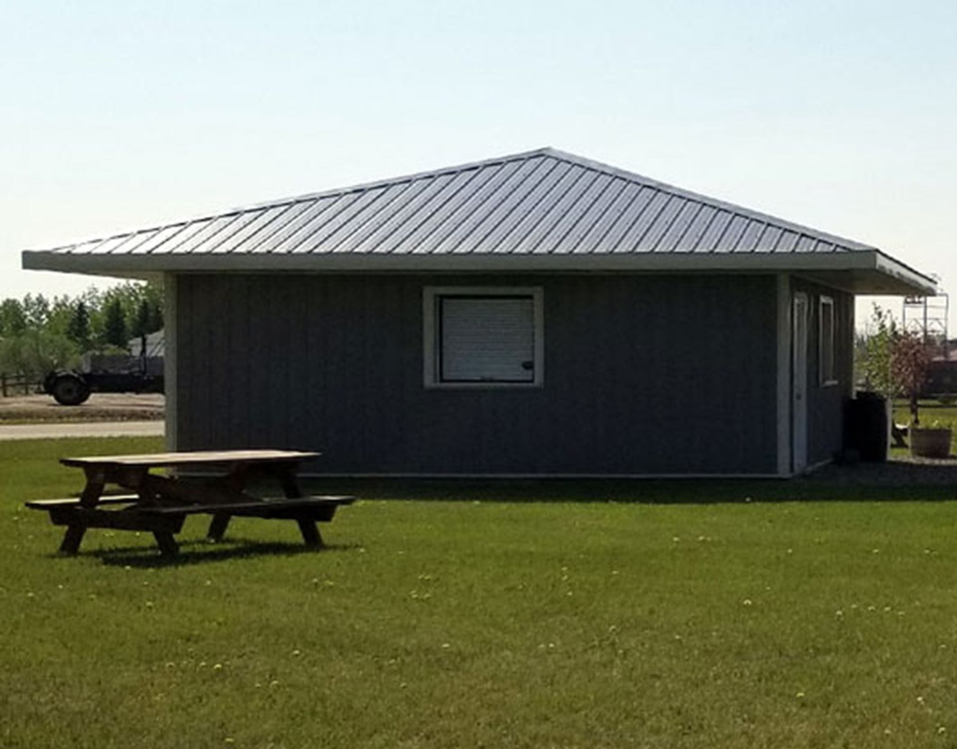 Grey building with a metal roof and a picnic table on the lawn.