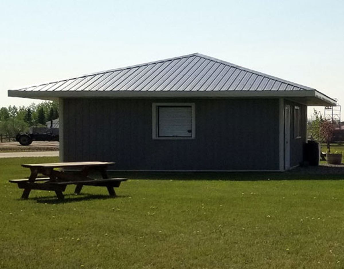 Grey building with a metal roof and a picnic table on the lawn.