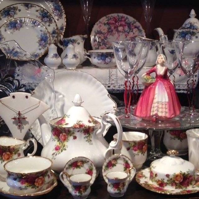 A collection of vintage china teacups, plates, glassware, and a porcelain figurine on display.