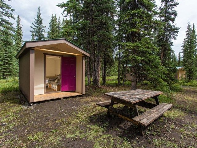 A cabin with the door open and picnic table out front.