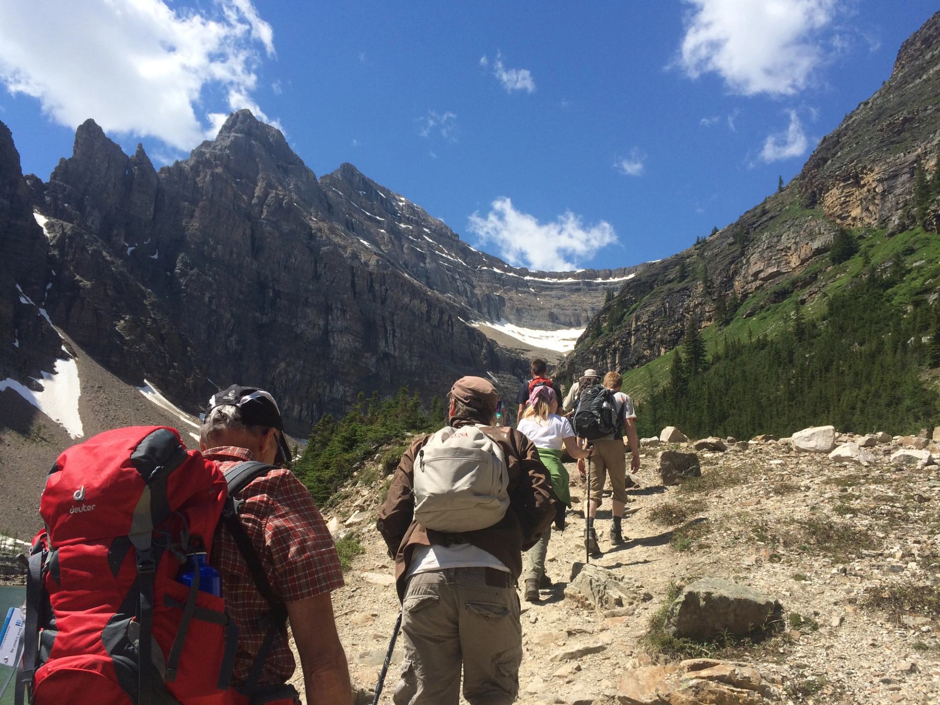 Line of hikers walking underneath steep cliff of mountains.
