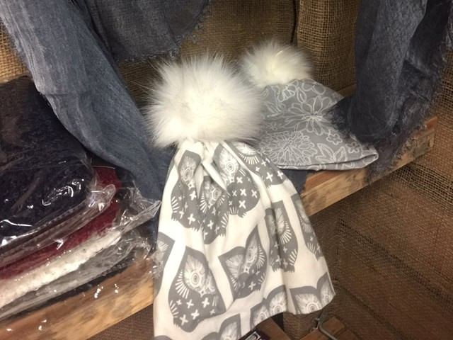 Grey owl-pattern scarf with white fur pom-poms on wooden display shelf.