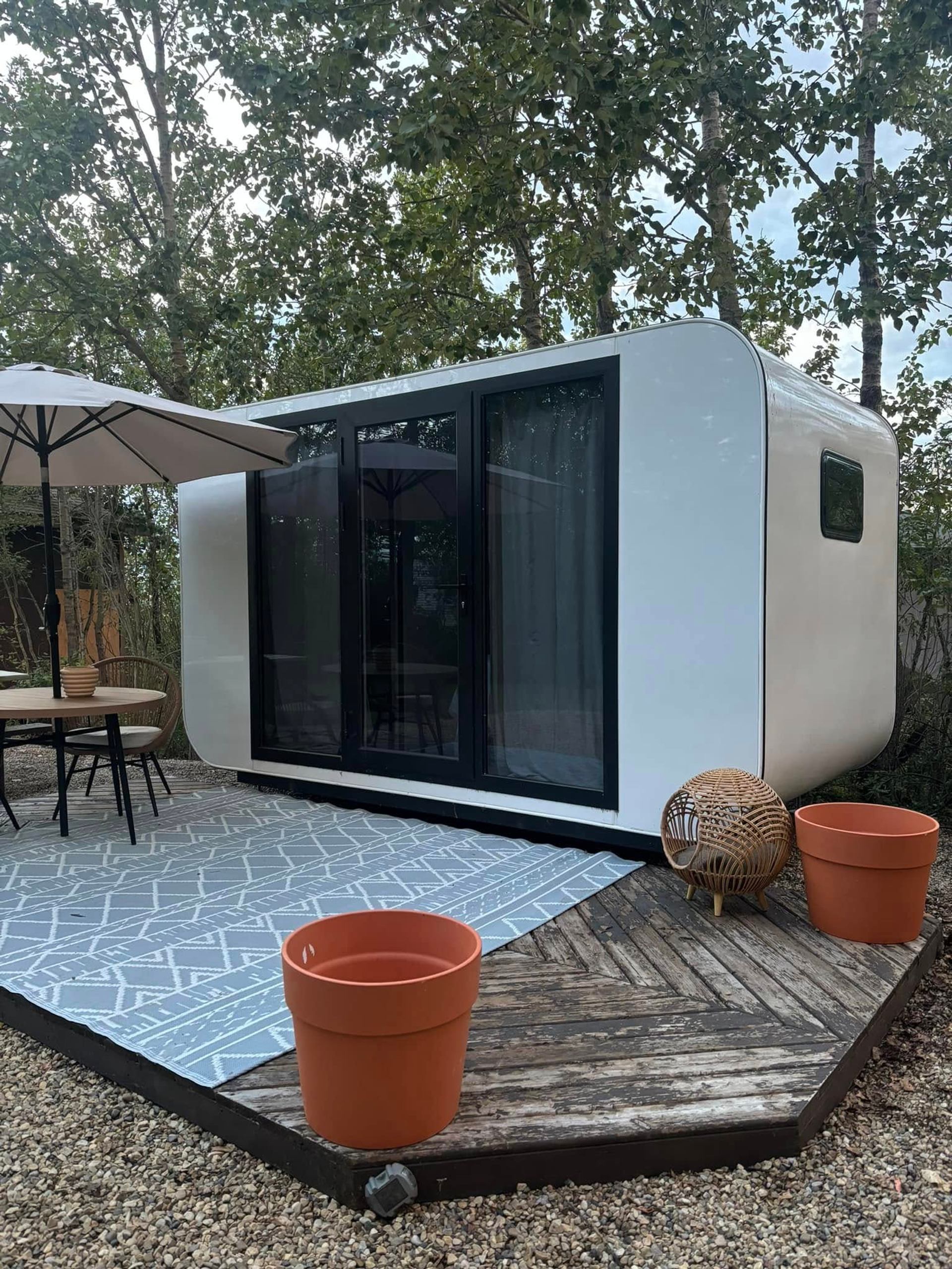 A modern cabin sits on a deck with outdoor seating surrounded by trees at Wilson’s Beach Campground.