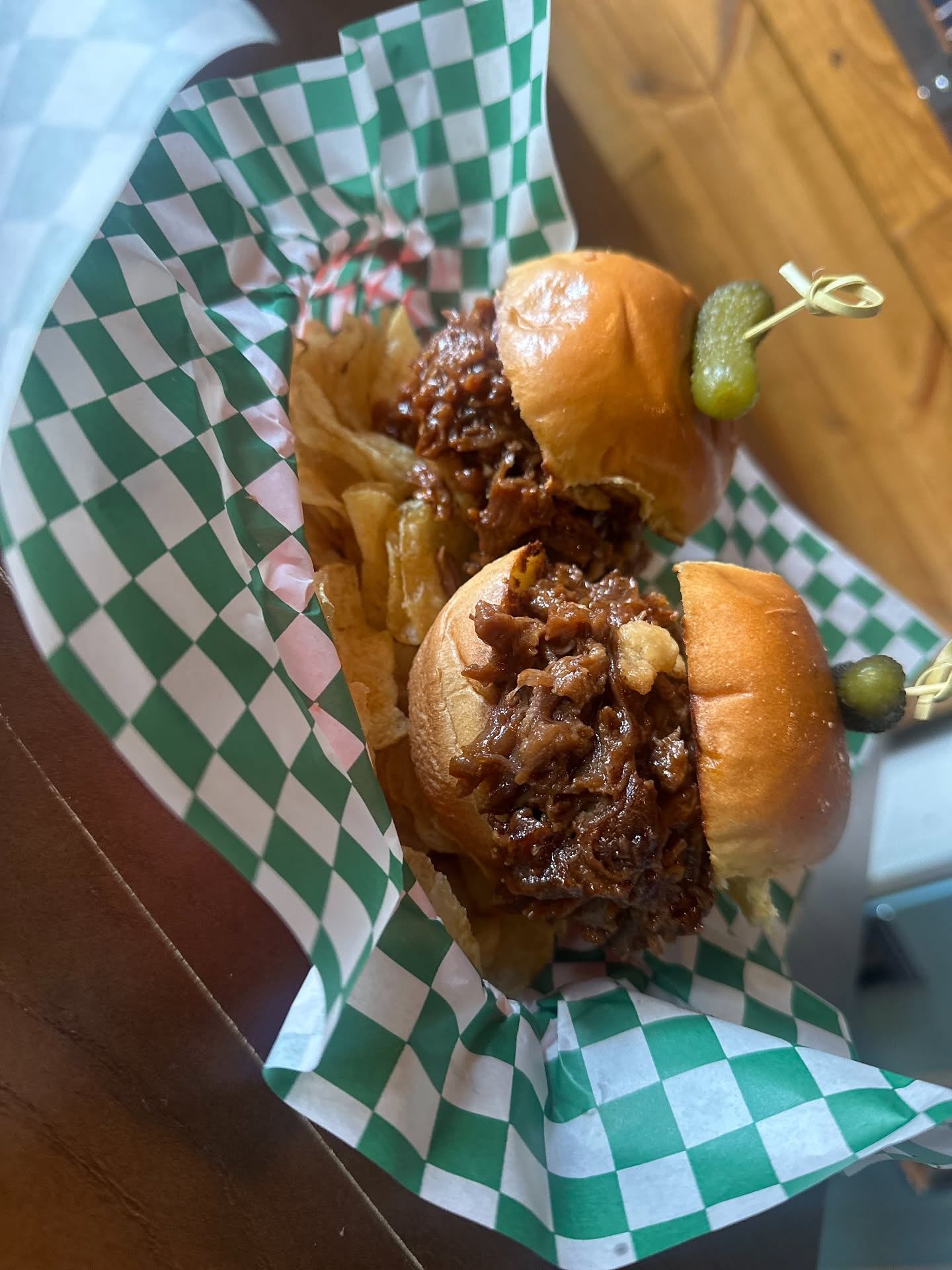 Two beef sliders topped with pickles are served with kettle chips in a basket-lined tray.