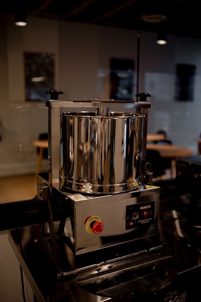 Stainless-steel coffee roaster with spigots and labels, inside a cafe setting.