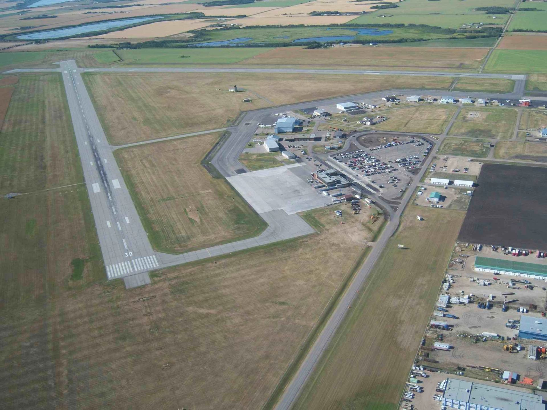 Aerial view of airport runway, terminal building and parking lot amid fields.