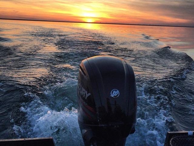 Boat with Mercury motor cruising at sunset, leaving a wake.