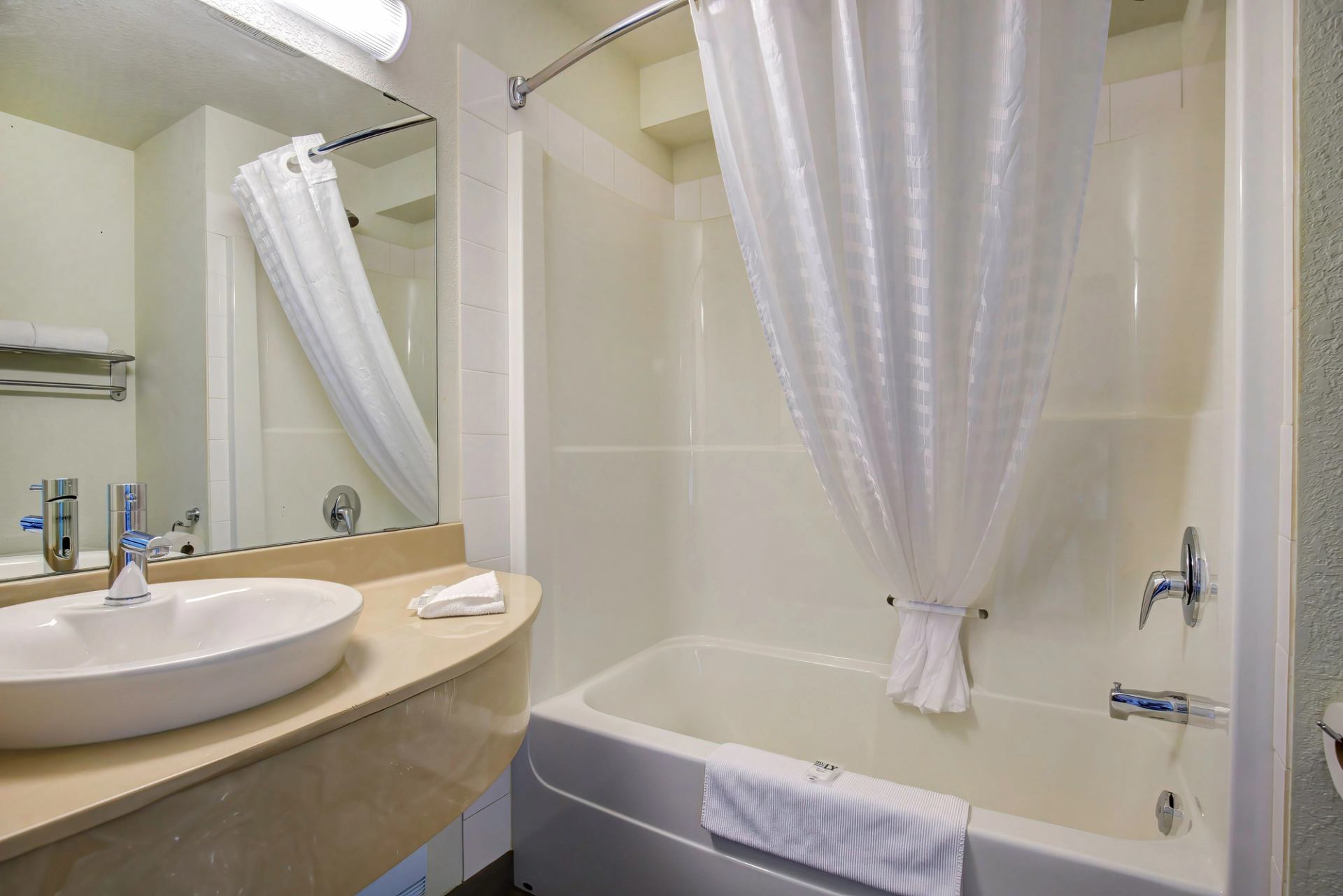 Bathroom featuring a bathtub with white curtain, countertop sink, and large wall mirror.