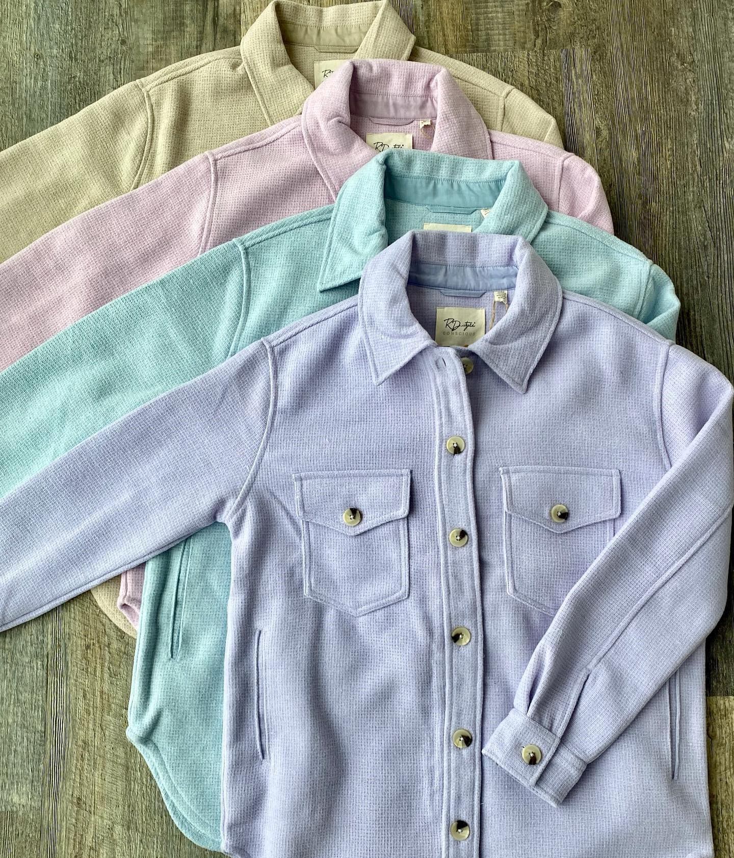 Collared button-up shirts stacked on wooden background, including lavender and light-blue styles.